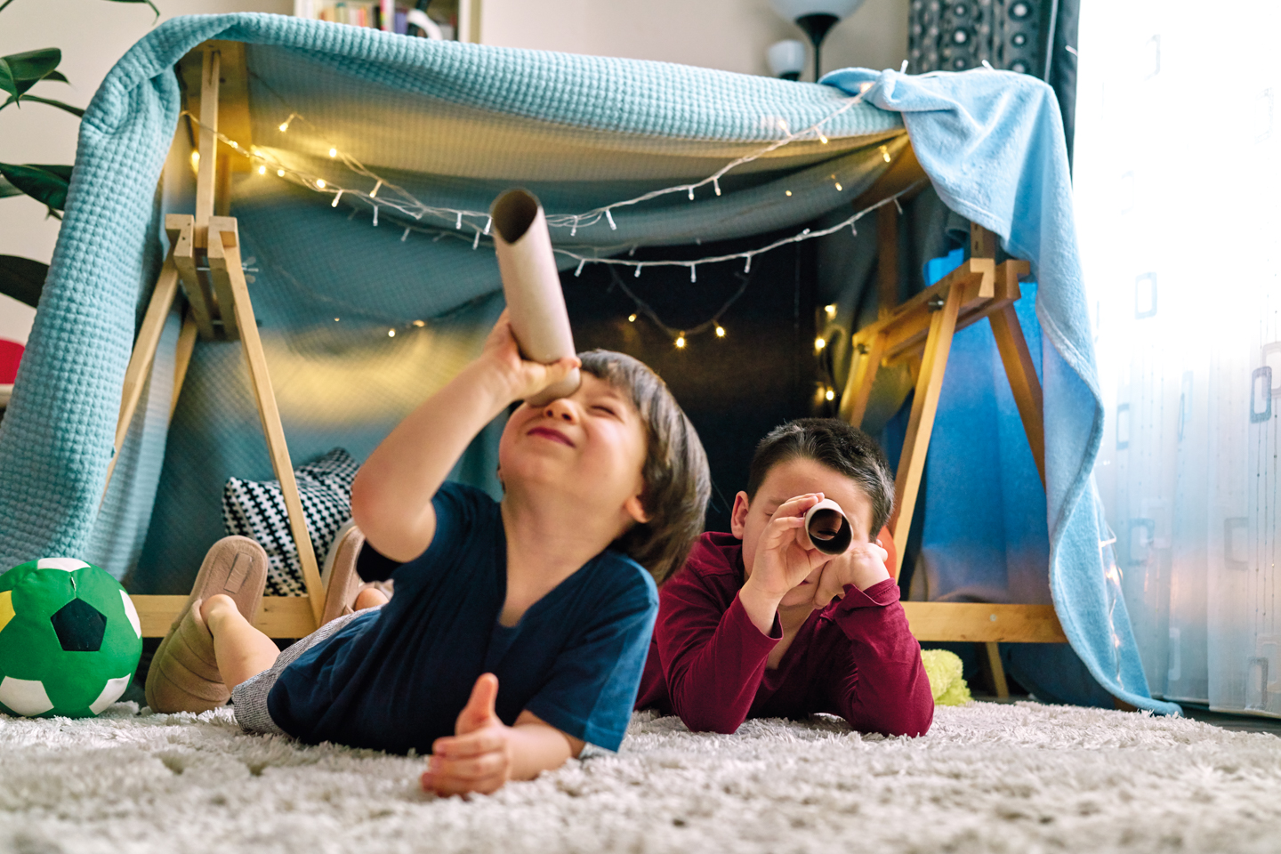 Two cute children making a camp and playing together in tent at home